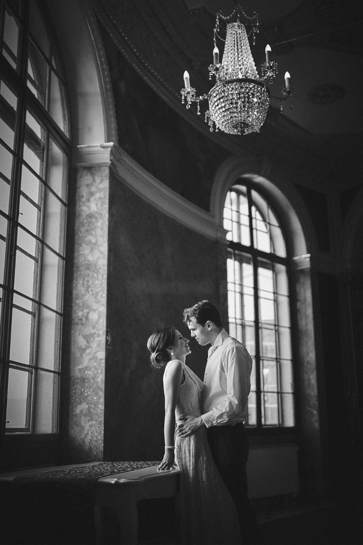 Monochrome imagae of couple quietly embracing near large windows of Chateau Liblice.