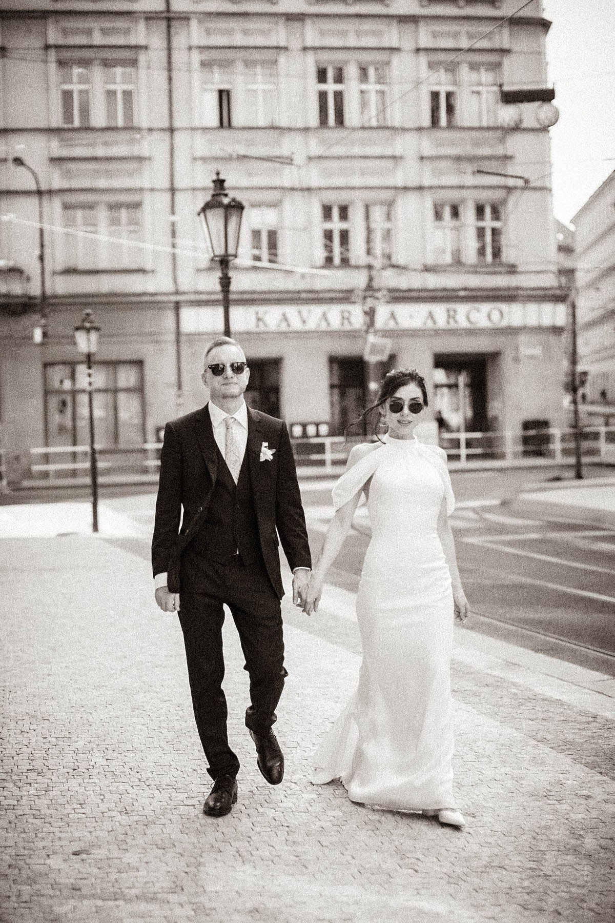 Bride and groom walking hand in hand through Prague's urban streets towards Masarykovo Train Station
