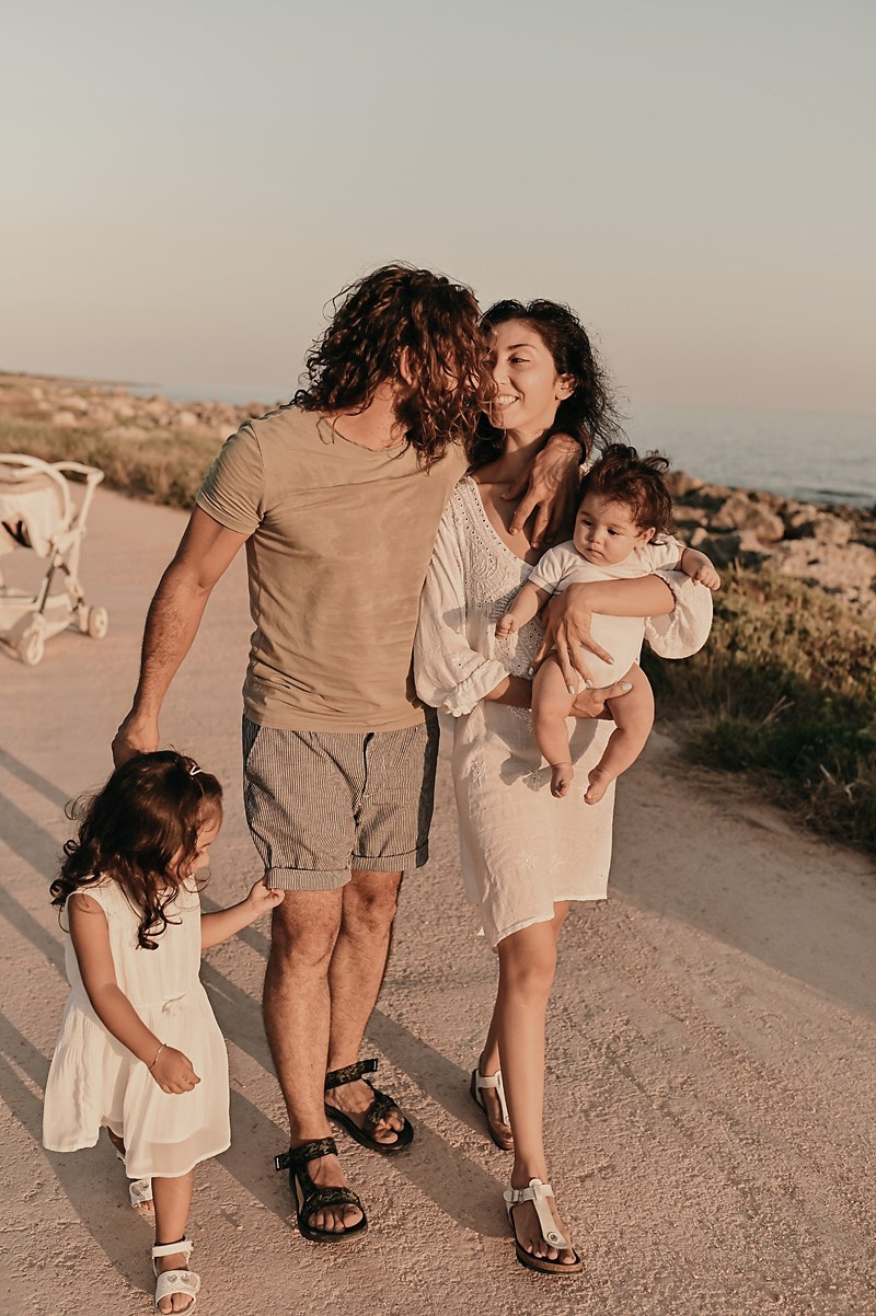 A family walking together by the sea, holding hands and smiling during golden hour.