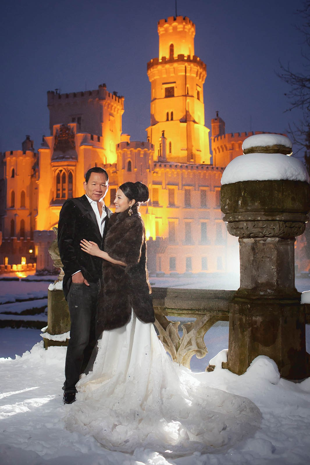 A stylish bride and groom pose for a nighttime portrait in the snow at Castle Hluboka.