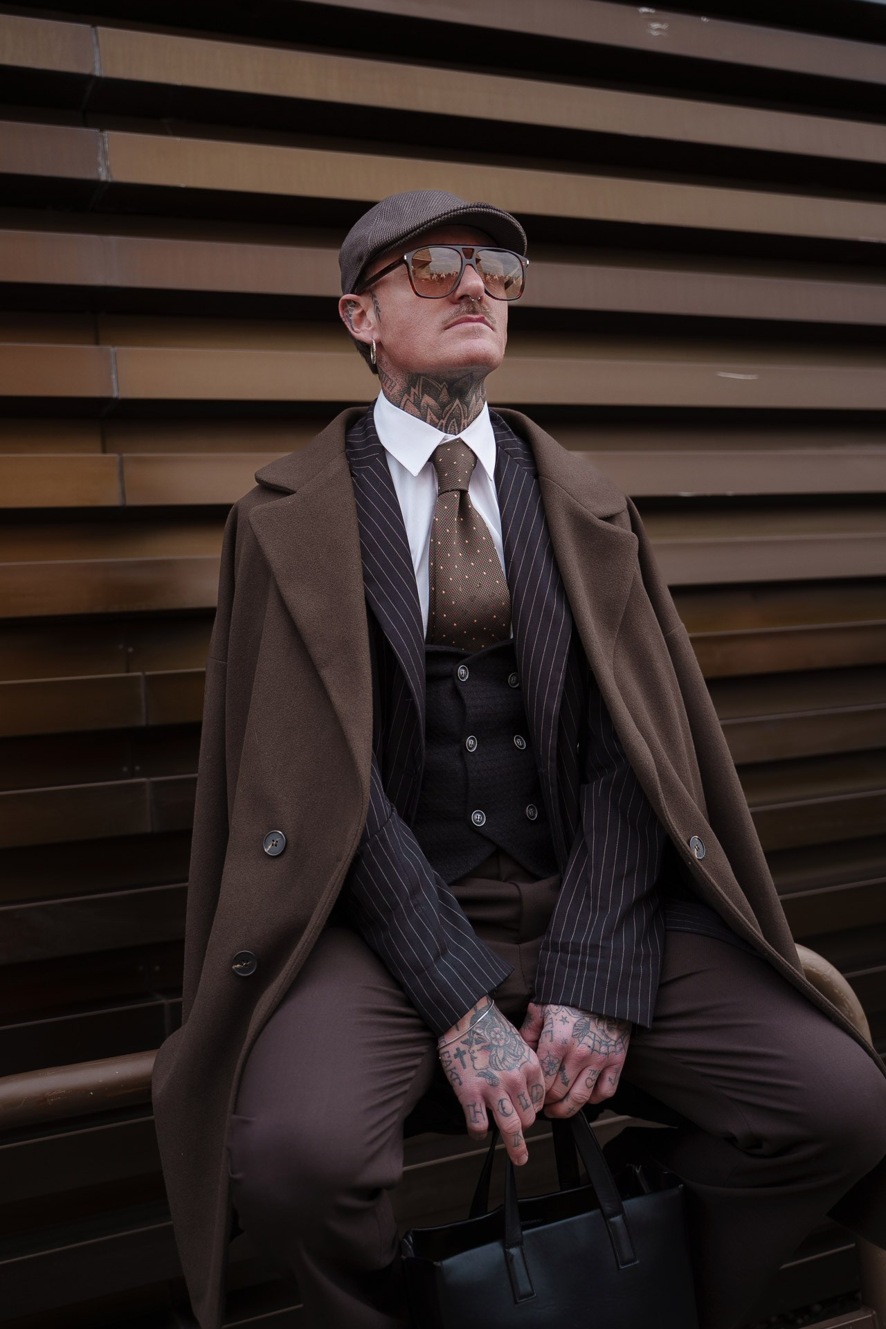 Man in brown suit and coat posing seated at Pitti Uomo Florence
