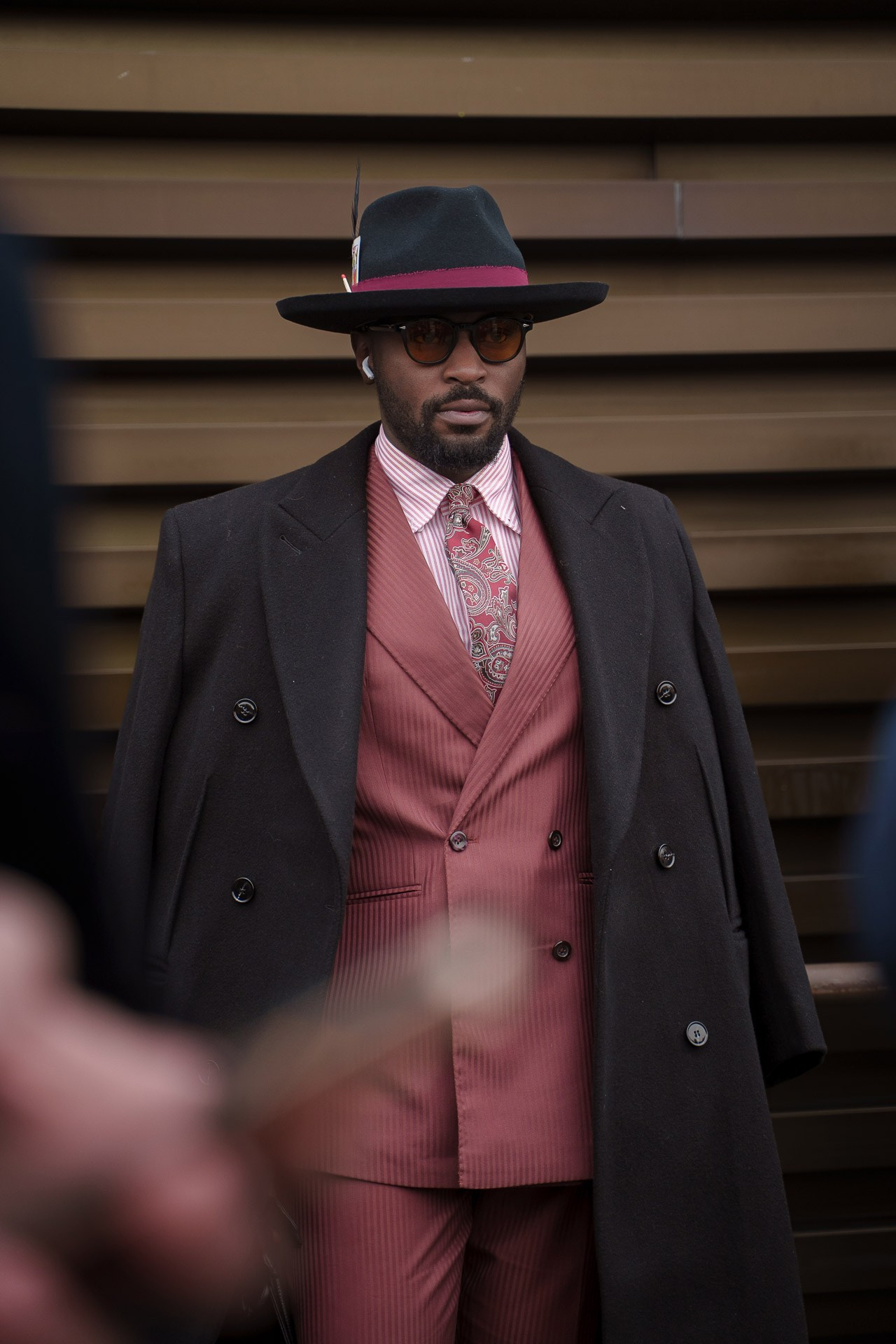 Man in pink suit and black overcoat wearing hat at Pitti Uomo Florence street style