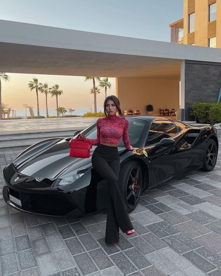 A beautiful girl sits on the hood of a black sporty expensive Ferrari against the backdrop of a Dubai building during Have a beautiful sunset