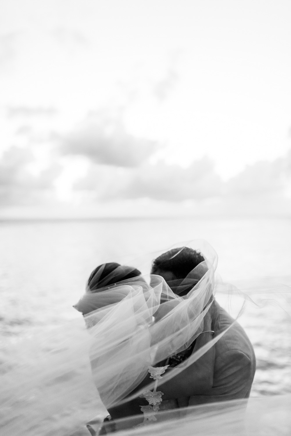 A fluttering veil covers the bride and groom kissing.