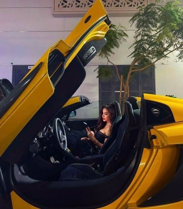 A model-looking girl is sitting in the cabin of an expensive sports car against the backdrop of a Dubai building
