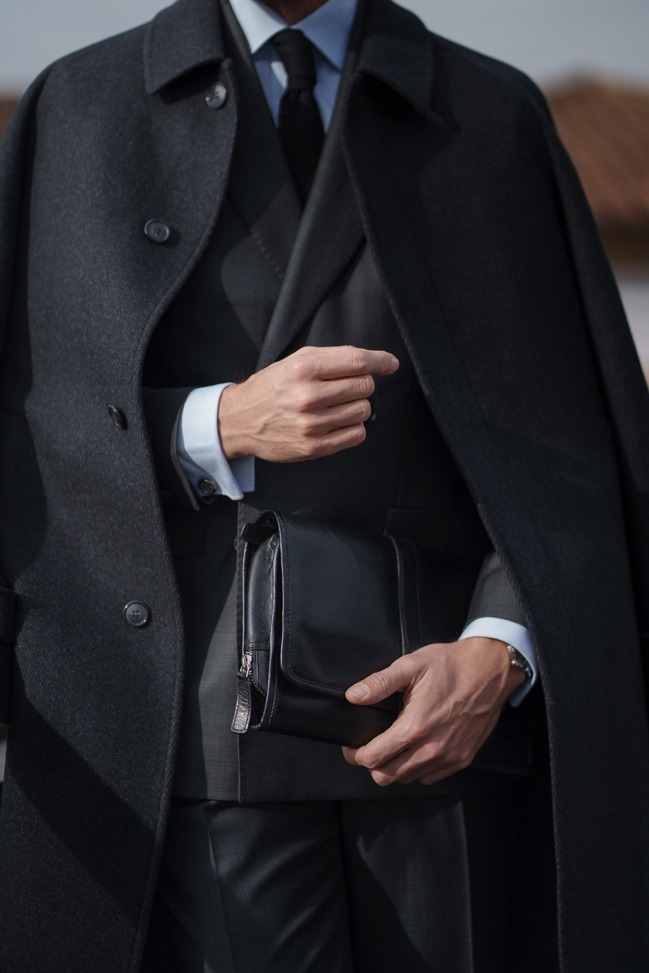 Close up of black overcoat and leather bag at Pitti Uomo street style