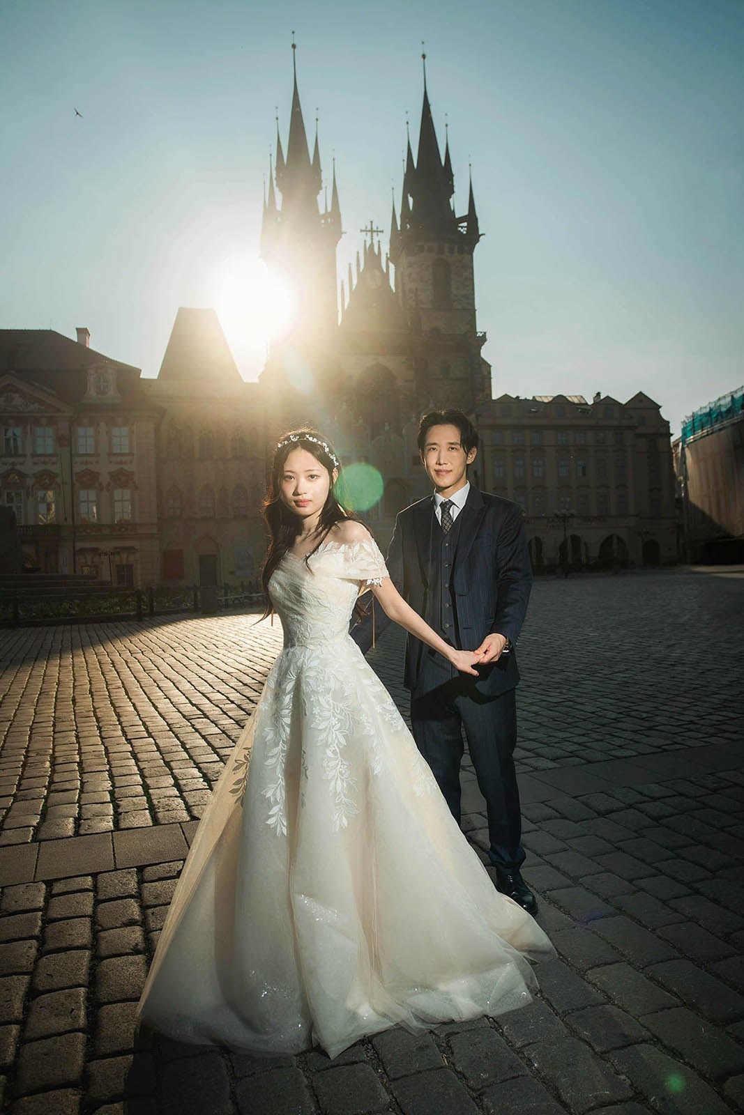 Newlyweds in the Old Town Square in Prague surrounded by lens flare breaking above the spires of Tyn Church