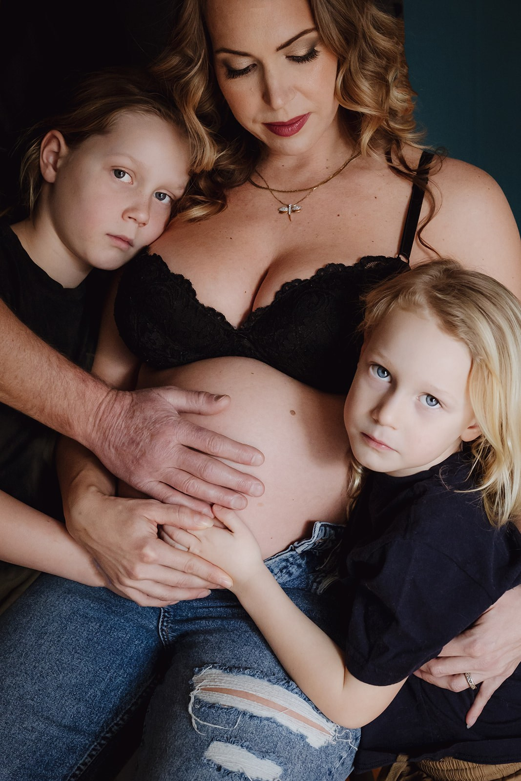 portrait of mother with pregnant belly and her two children leaning on her belly