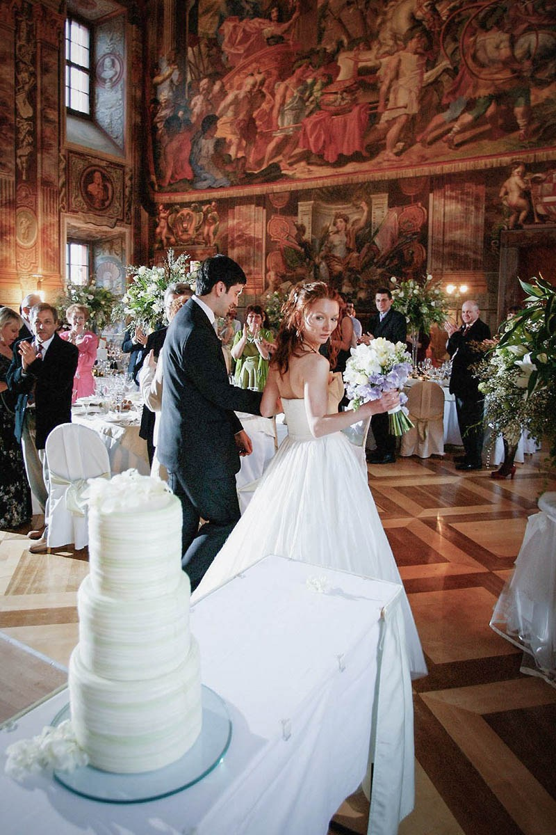 A towering wedding cake captures the gaze of the red-haired Russian bride as she enters the ballroom of the Troja Palace in Prague.