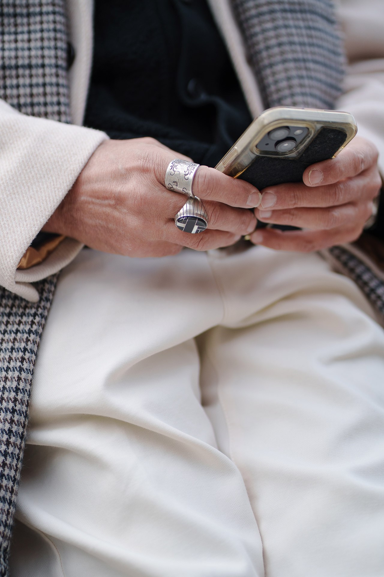Close up of man holding smartphone wearing rings and tailored trousers at Pitti Uomo 109 Florence