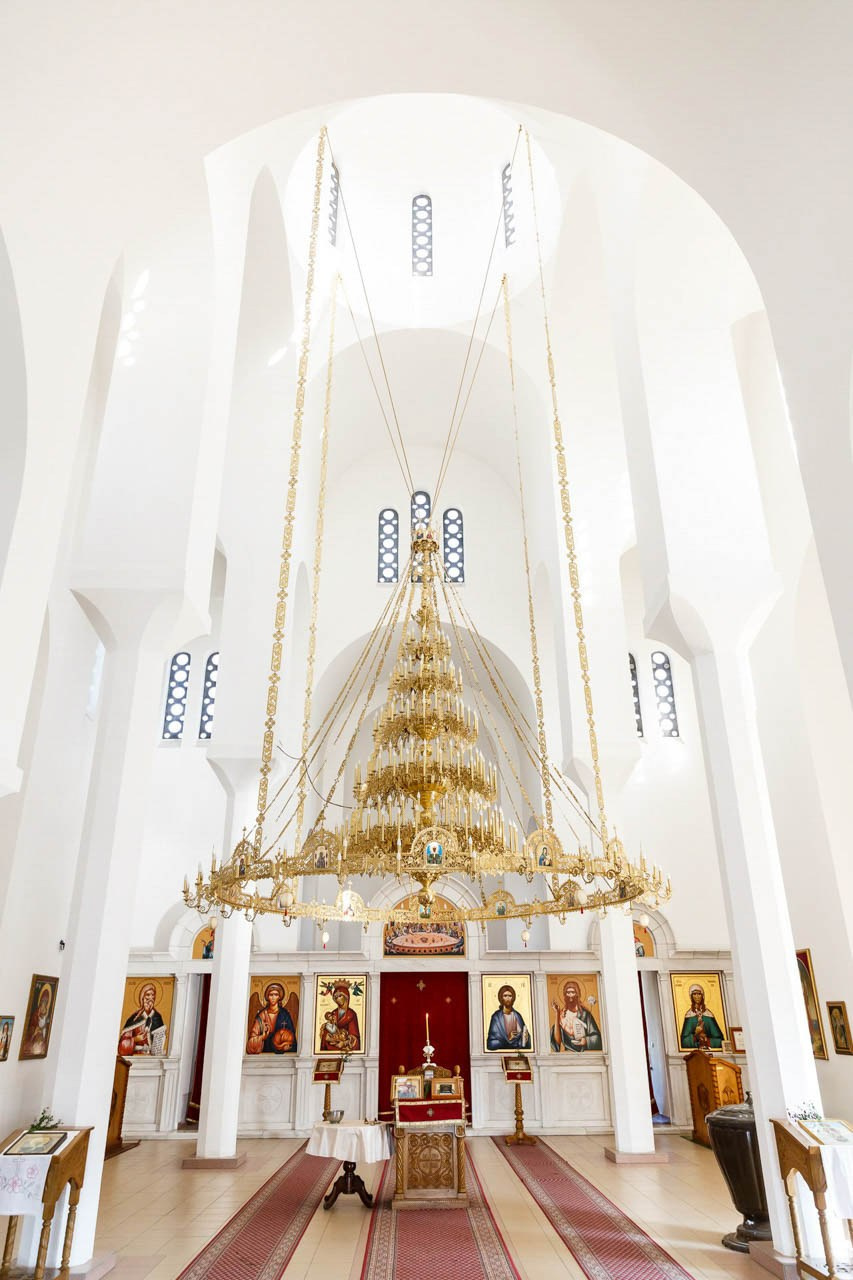Impresivan enterijer pravoslavne crkve sa pozlaćenim lusterom i ikonama.