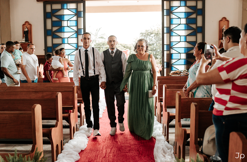 Entrada triunfal dos noivos na cerimônia de casamento, rodeados por familiares e amigos.