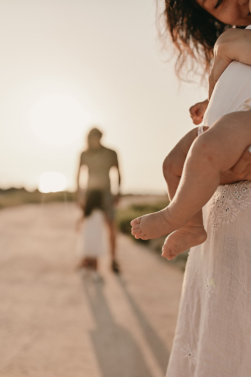 A warm close-up of a baby’s feet in mother’s arms, with the rest of the family softly blurred in the background.