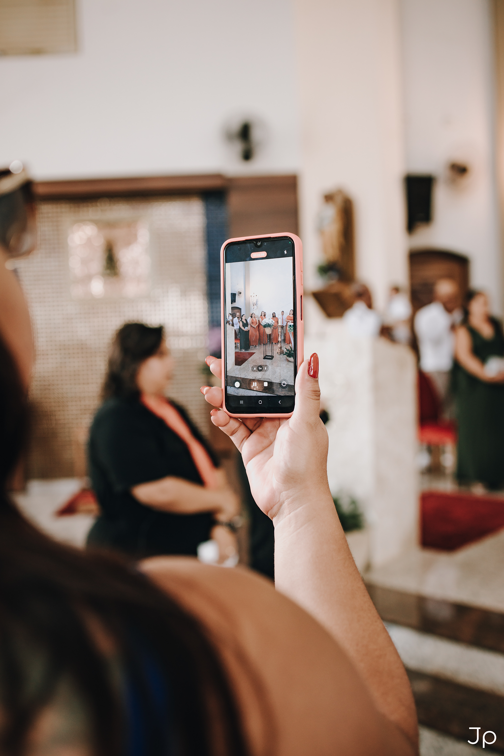 Mão de convidado fotografando cerimônia de casamento com smartphone, retratando memórias importantes.