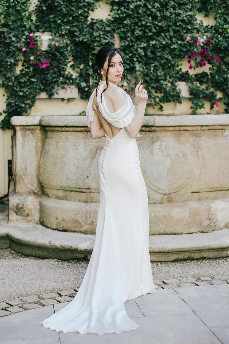 Striking brunette bride with a cigarette looks over her shoulder towards the camera's gaze as she strikes a sexy pose.