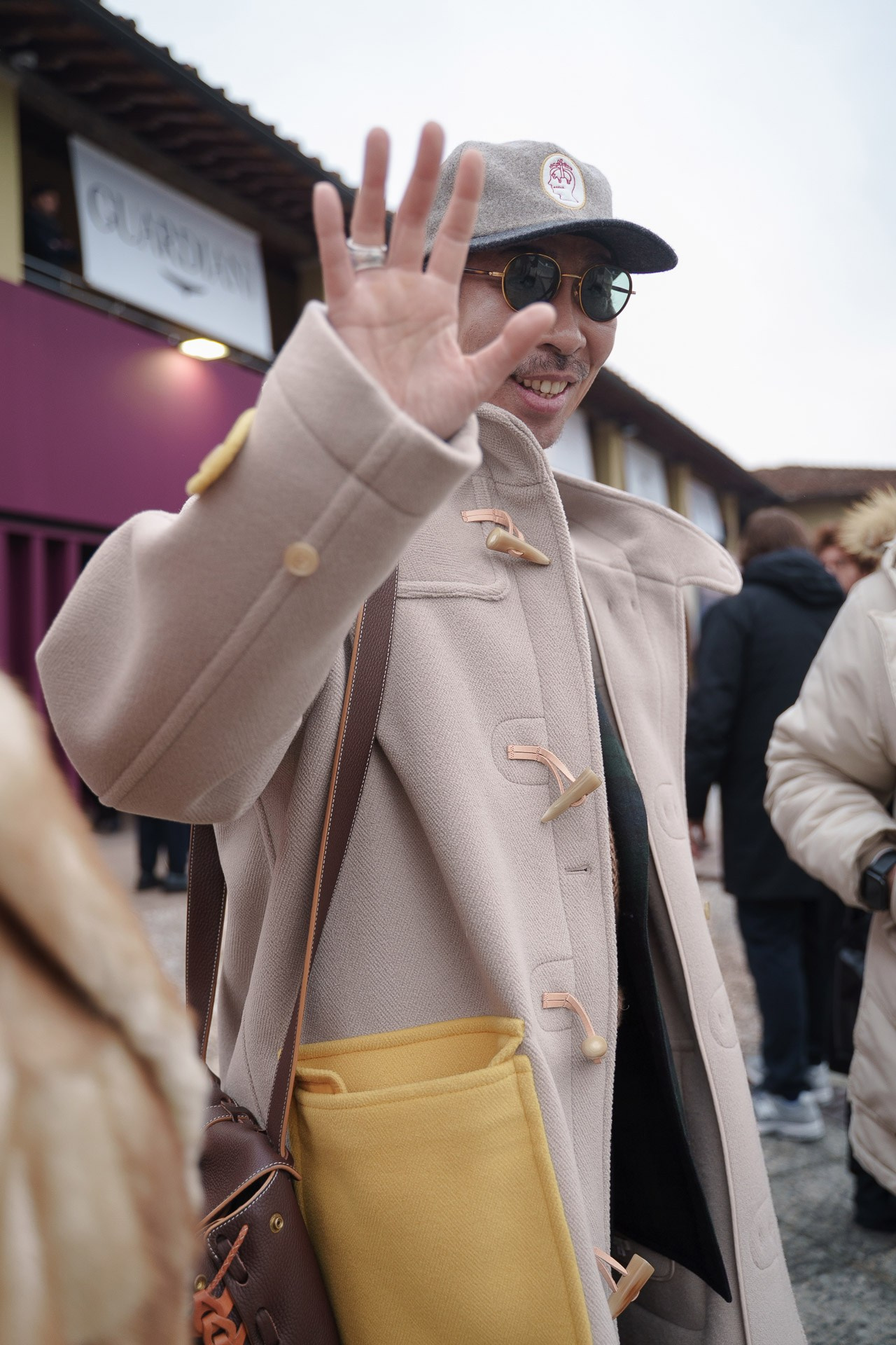 Man in beige duffle coat waving at Pitti Uomo Florence street style