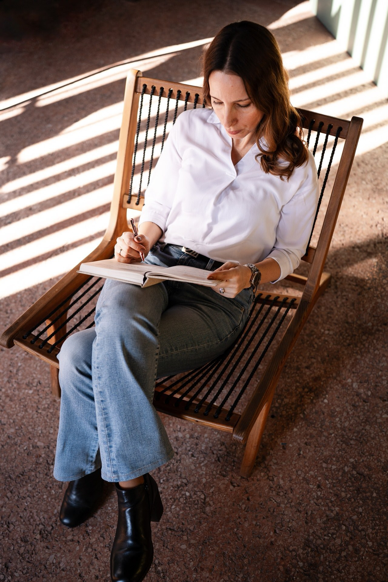 žena sedi u fotleji sa interesantnom snekom sunca na podu, drži rokovnik u rukama snimljeno odgore