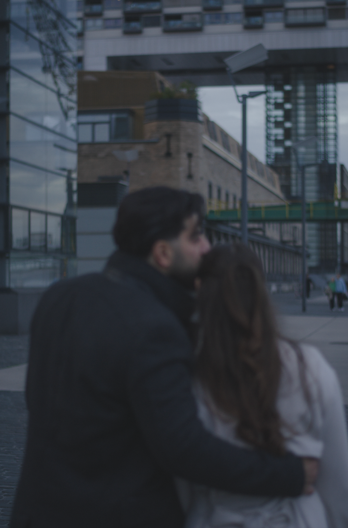 Foto eines verliebten Paares auf dem der Mann die Frau auf den Kopf küsst mit urbanem Hintergrund