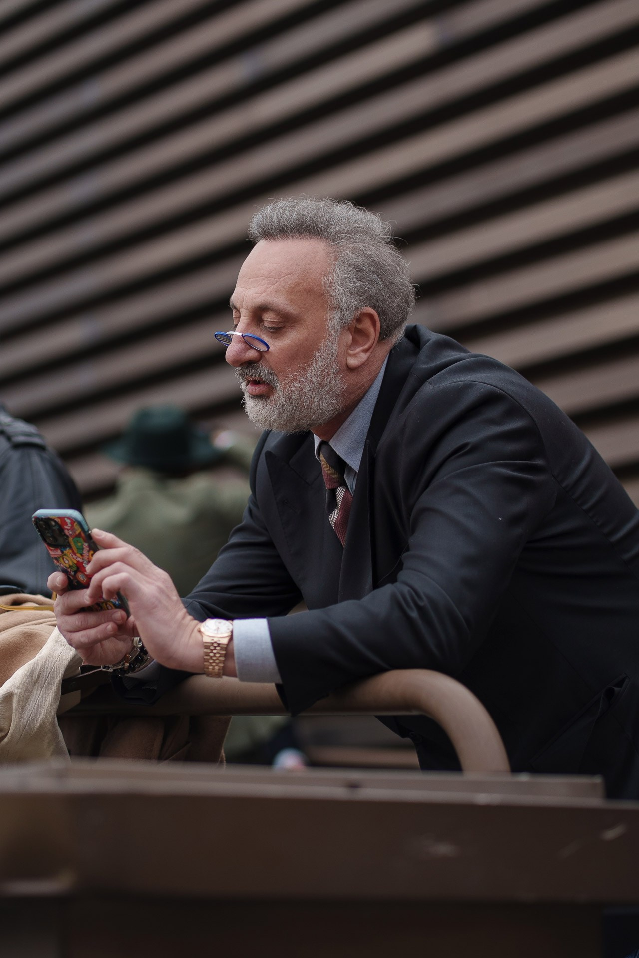 Man in black suit checking phone while sitting at Pitti Uomo Florence