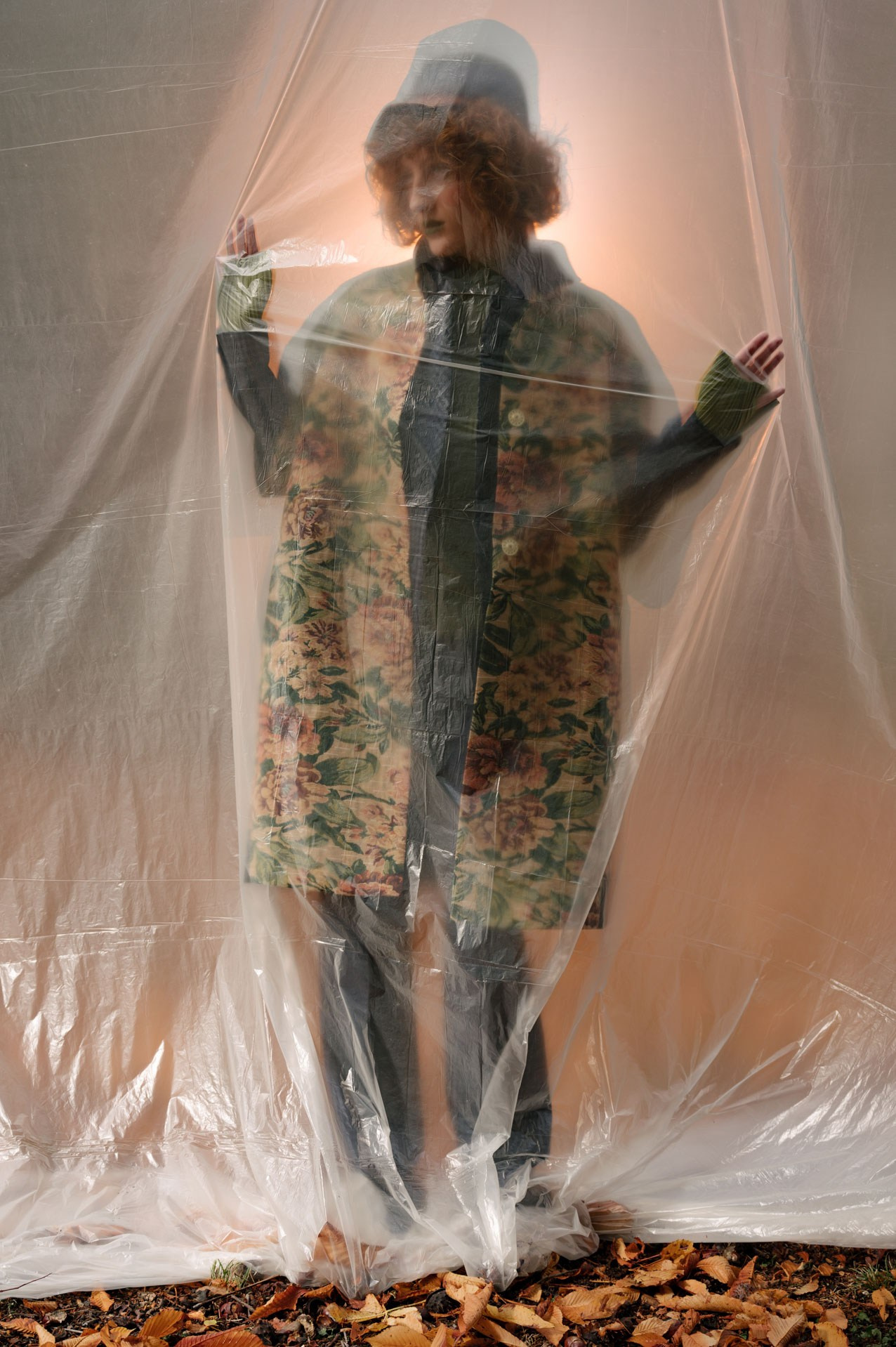 Artistic fashion portrait in Dubai of a model standing behind transparent plastic sheet wearing floral coat and bucket hat, autumn concept