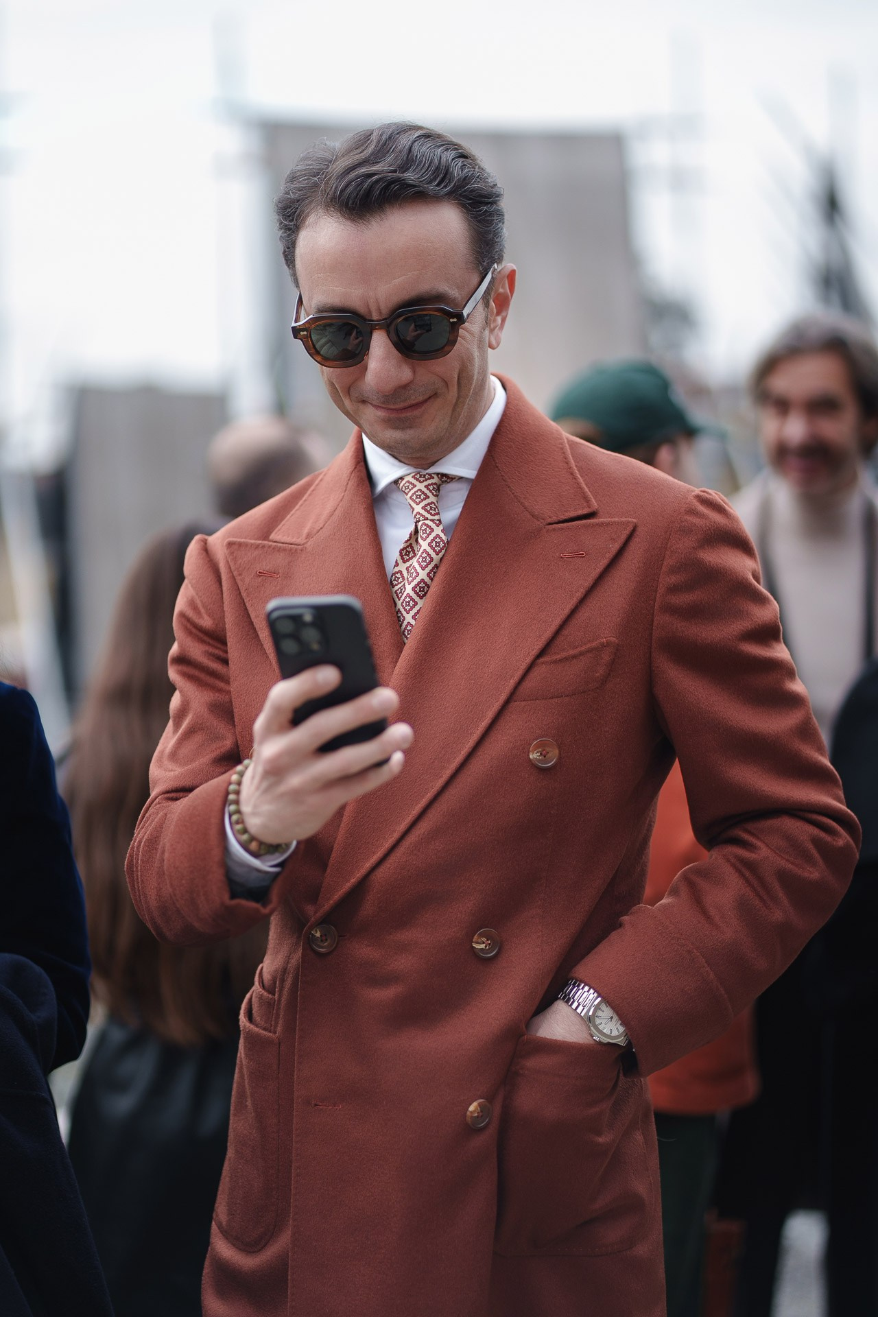 Man in rust colored double breasted coat checking phone at Pitti Uomo 109