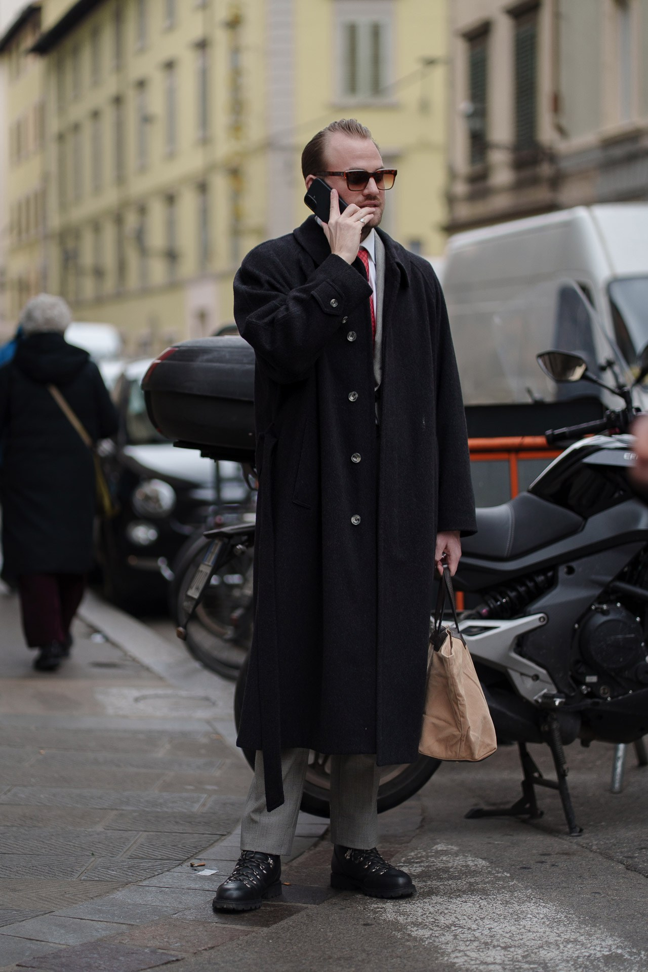 Man in long black coat talking on phone outside Pitti Uomo 109 in Florence street style