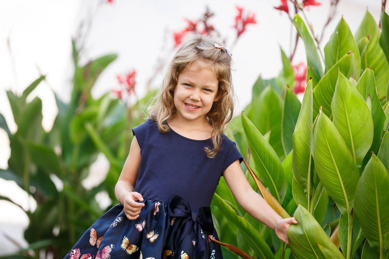 Nasmejana devojčica u bašti sa cvećem – portret posle ceremonije krštenja.