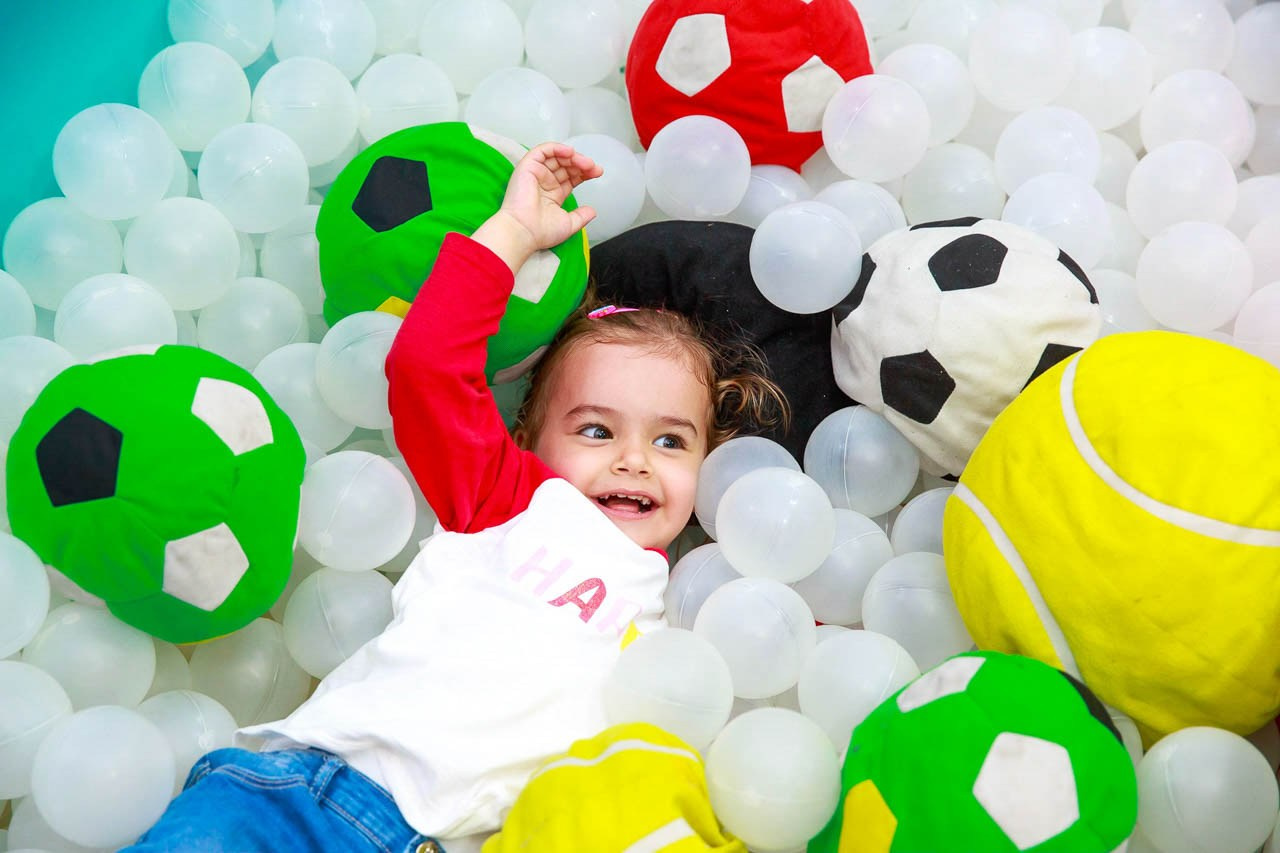 Dečak u bazenu sa lopticama u obliku fudbalskih lopti.