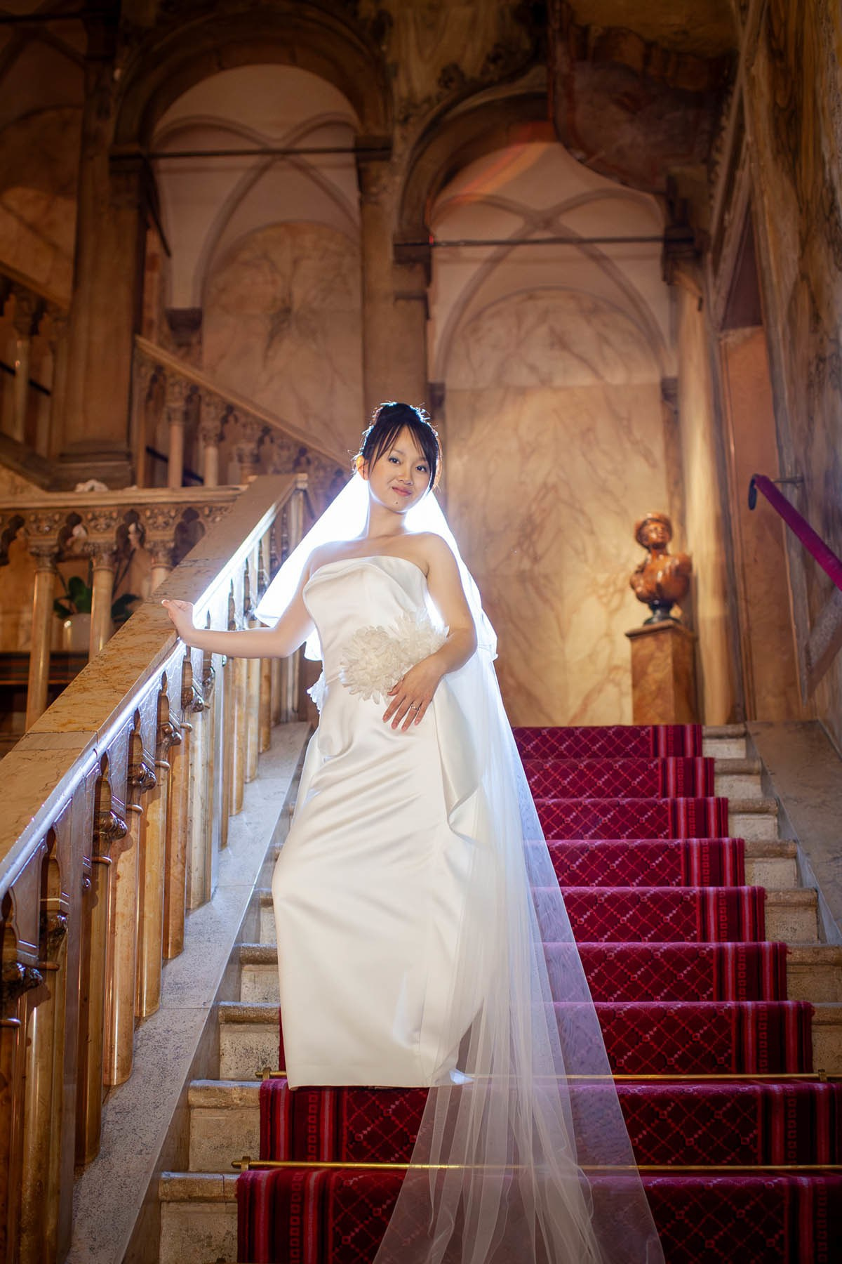 Smiling Thai bride in white wedding dress descending steps inside historic Hotel Danieli in Venice.