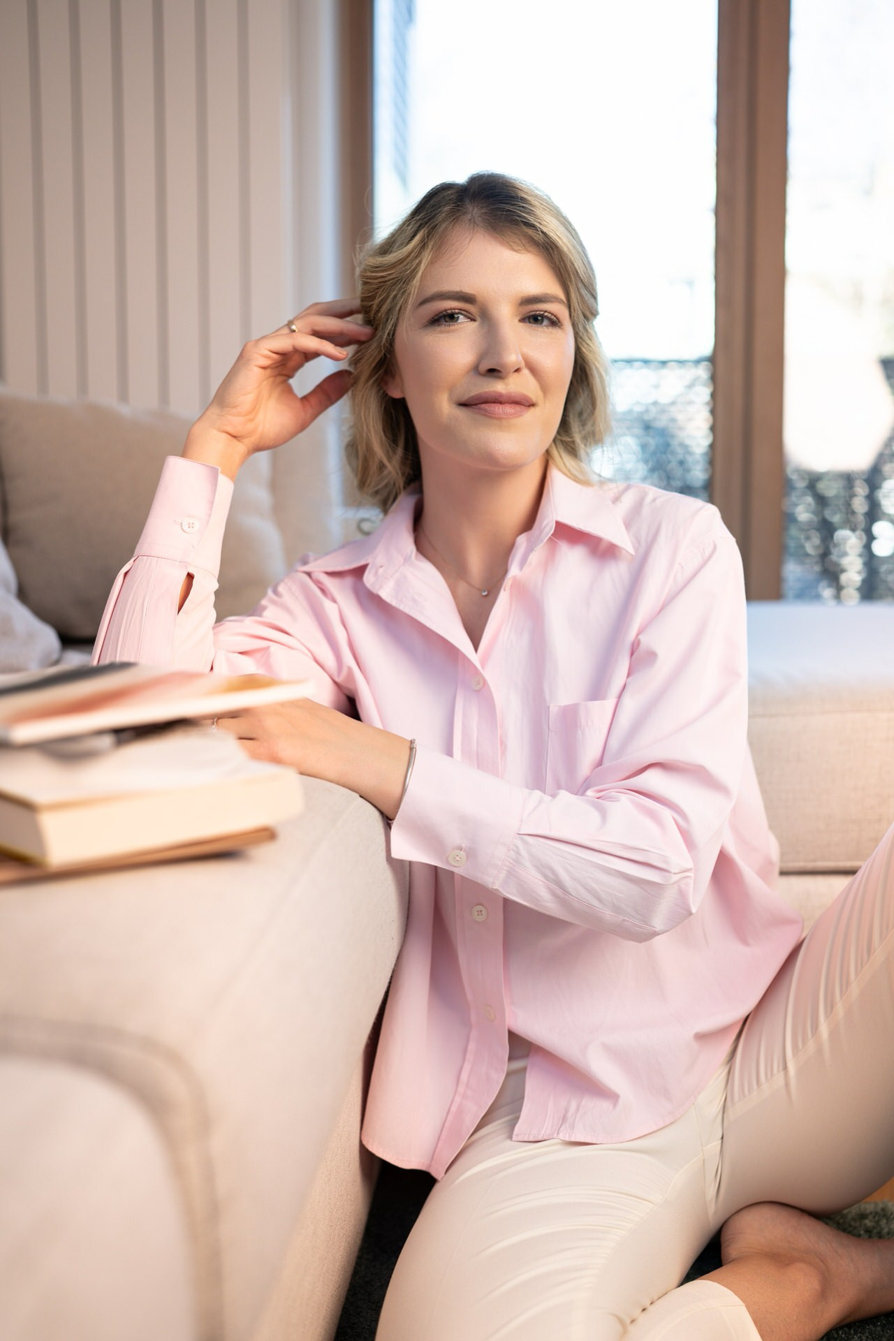 mlada žena sedi na podu naslonjena na garnituru pridržavajući glavu rukom ispred nje su knjige