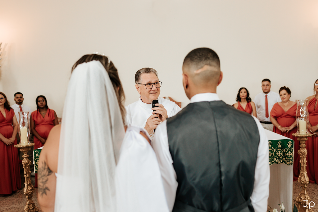 Casal recém-casado posando com o padre ao fundo, registro de felicidade e união no casamento.