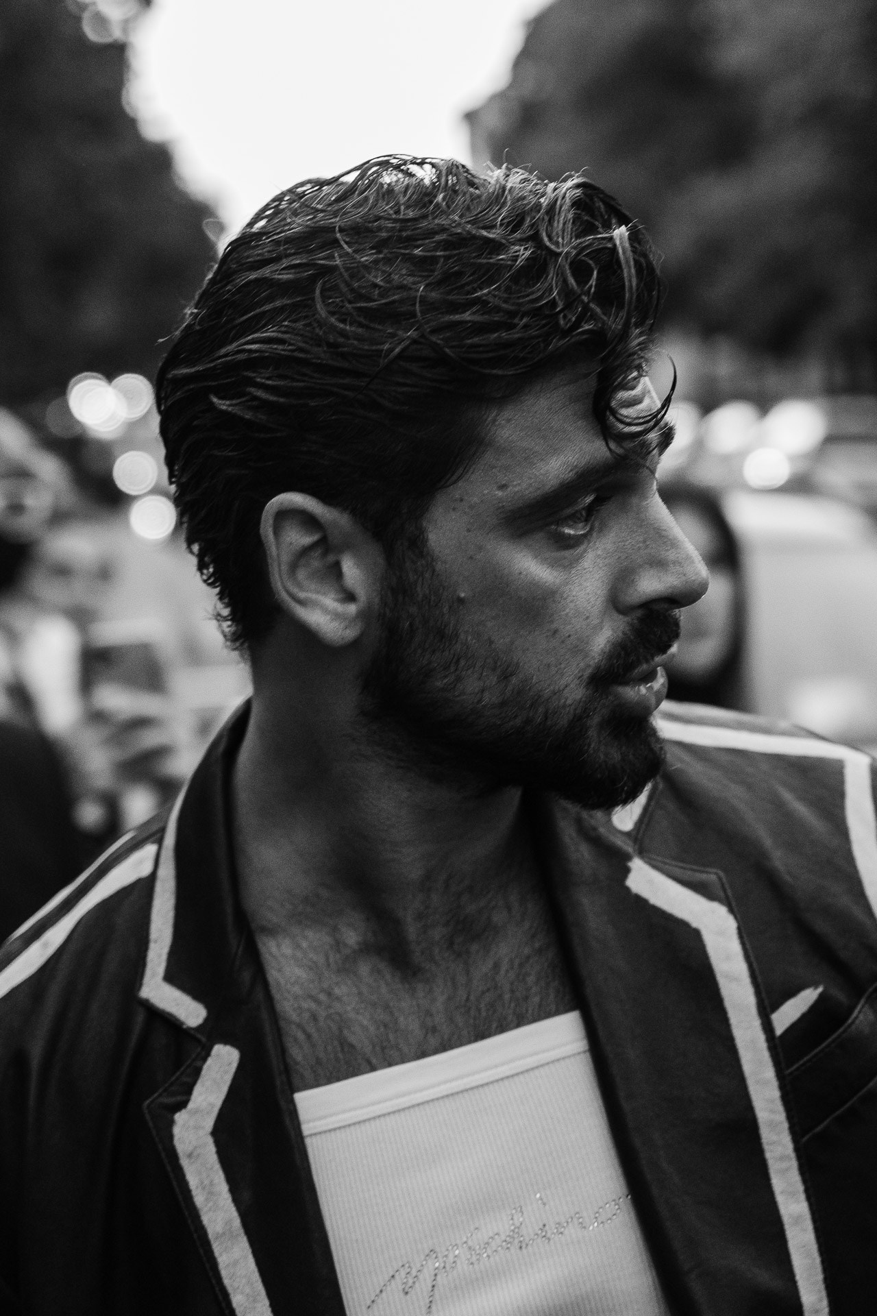 Actor Michele Morrone attending Milan Fashion Week. A cinematic black and white profile shot highlighting a tailored Moschino blazer with contrast piping and a branded tank top.