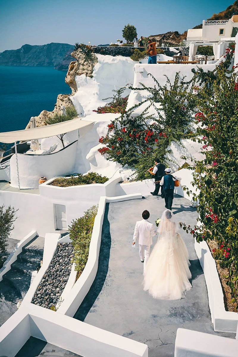 Musicians leading newlyweds along Santorini cliffs