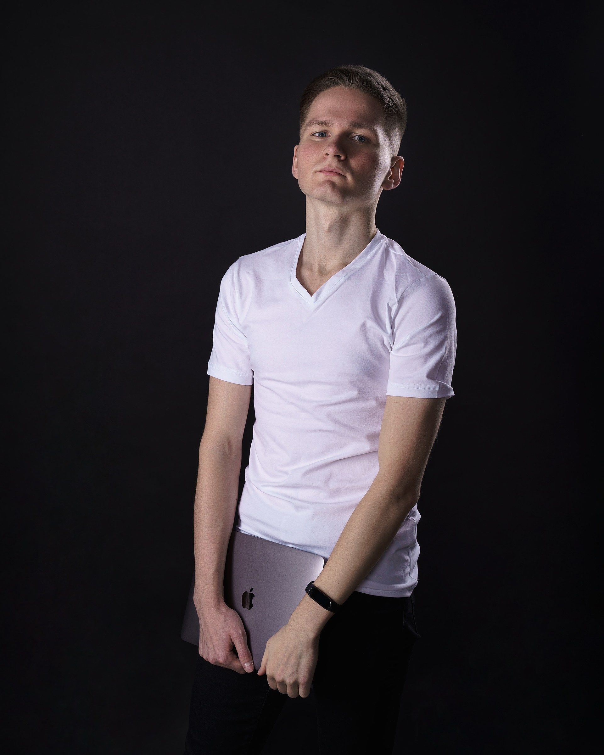 Young man in a white t-shirt holding a laptop against a black background in NJ