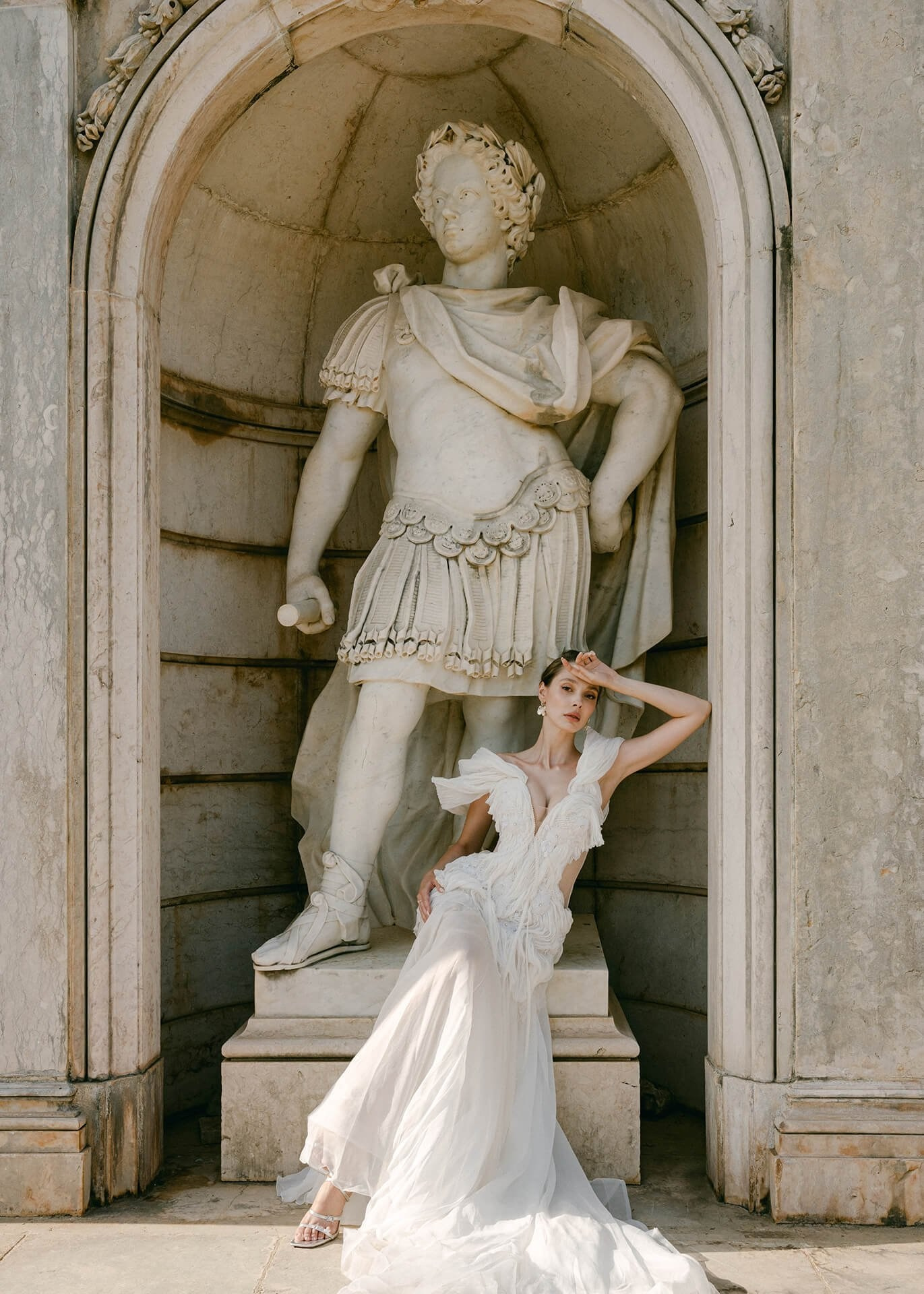 Woman in a flowing white gown posing beside a classical marble statue at a historic Italian villa on Lake Como