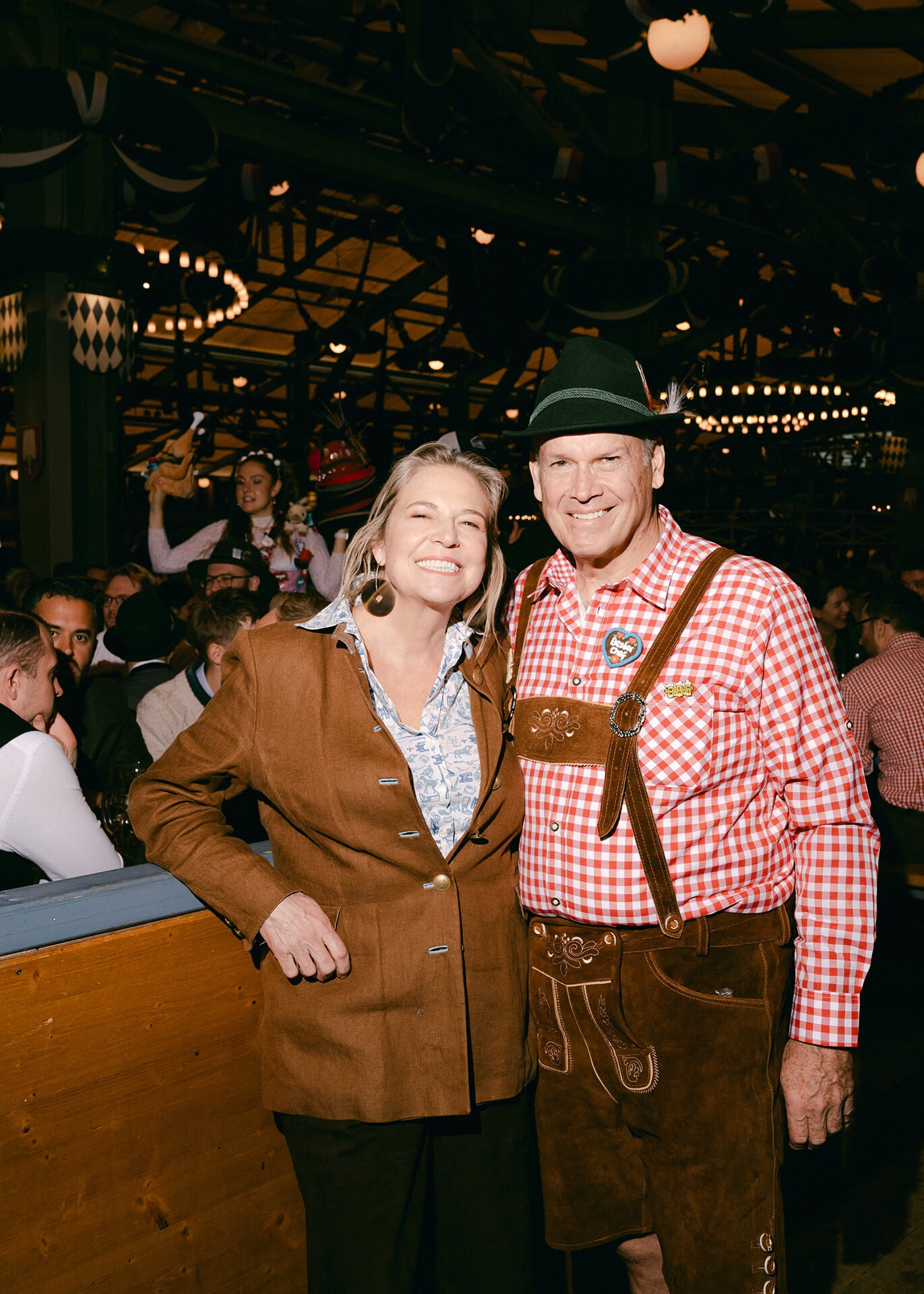 Paar in Lederhose und bayerischer Tracht lächelt im vollen Oktoberfest-Bierzelt in München