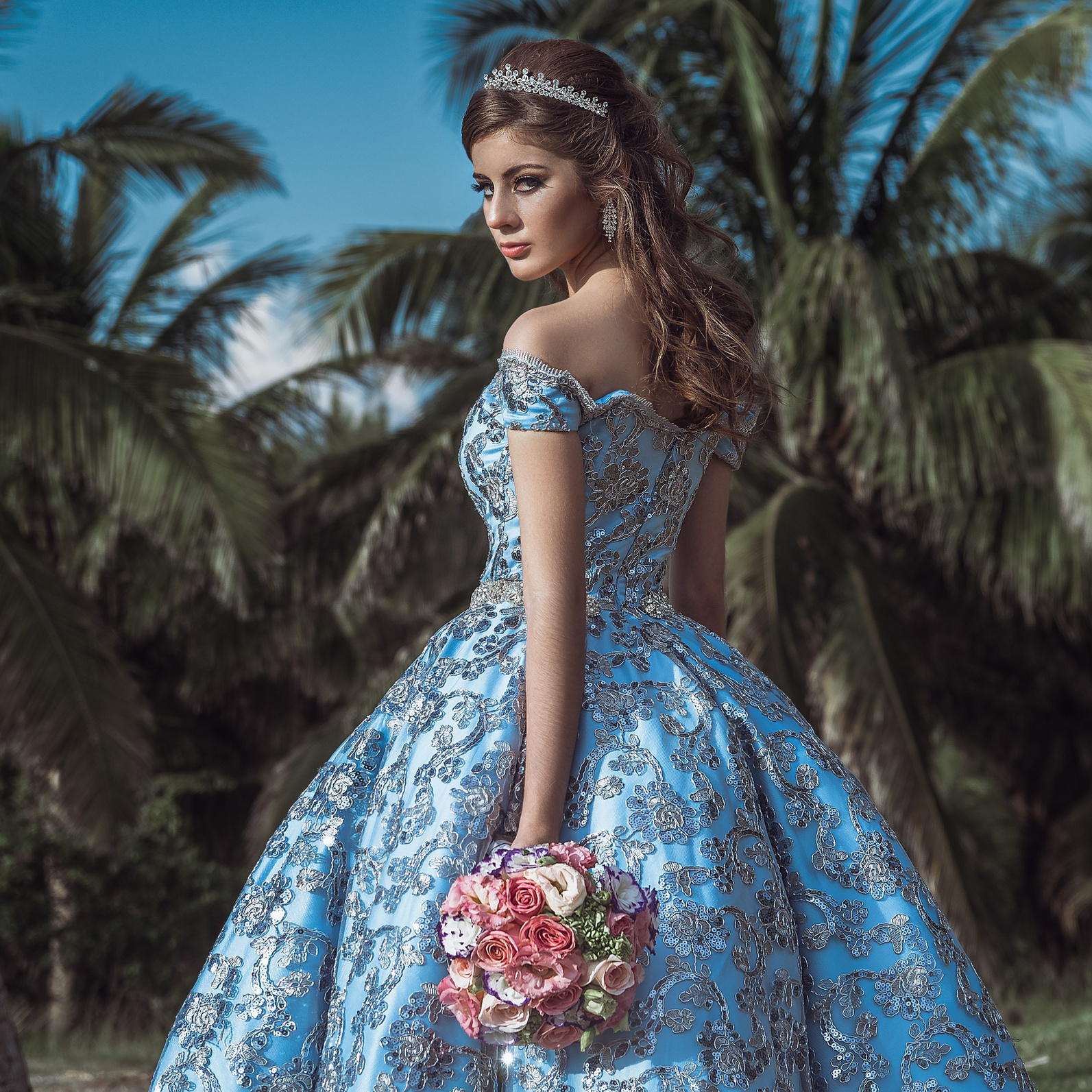 Quinceañera con vestido azul bordado frente a palmeras, fotografía de XV años en México, fotógrafo Carlos RaGo Coatzacoalcos