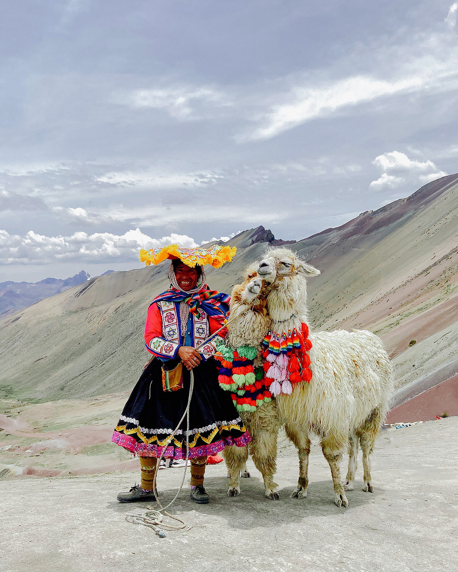 Традиционно одетая перуанская бабушка держит в руках две ламы и смотрит в камеру фотографу. 