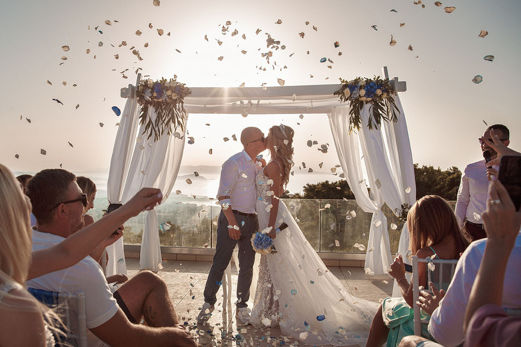 Молодоженов осыпают лепестками роз в арке на свадебной церемонии на Крите. Фотограф, свадьба в Греции.