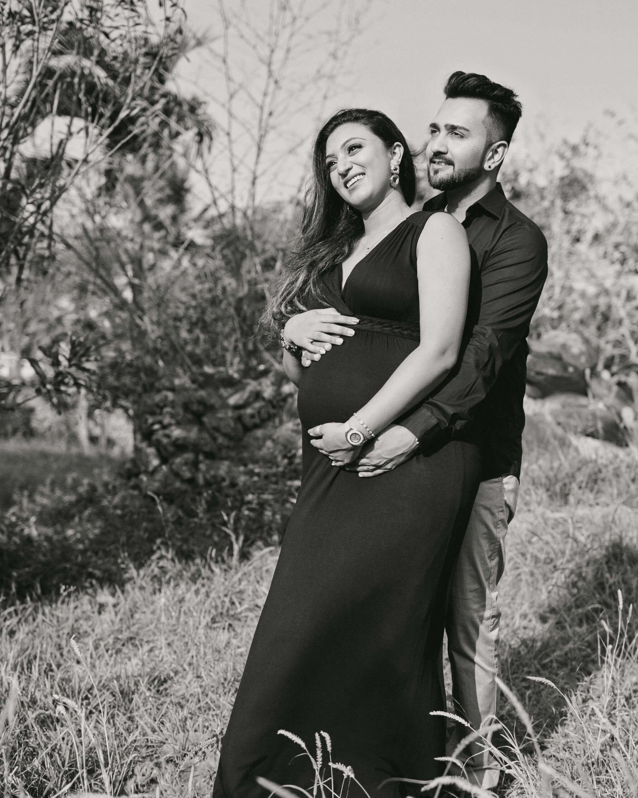 Elegant black & white maternity portrait of woman posing near tall grass, styled for classic maternity albums.
