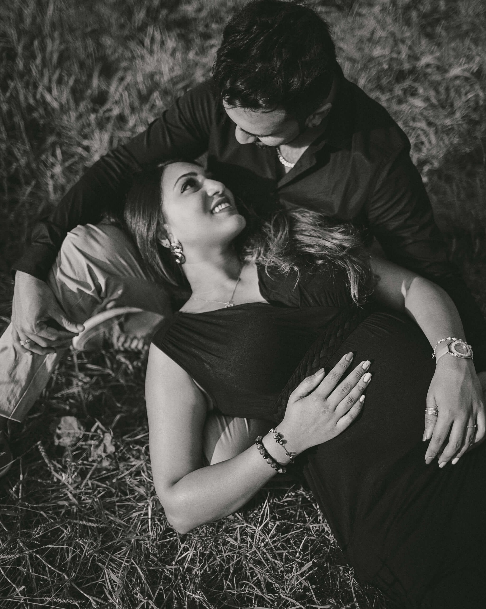 Elegant mother-to-be in formal black dress smiling with her hands on belly, captured in old film style.