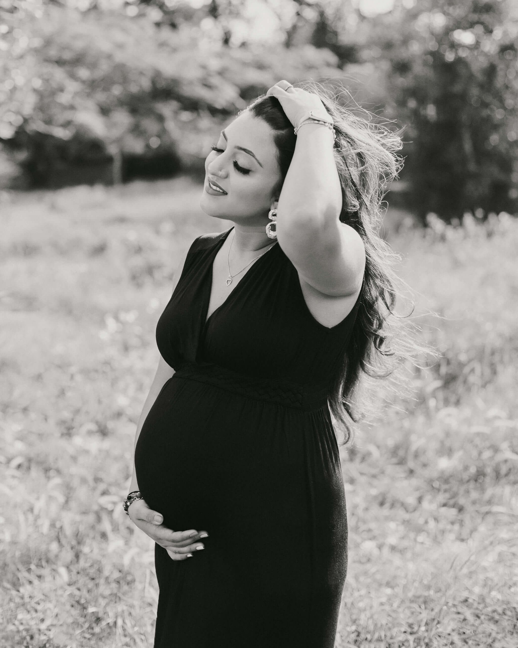 Vintage black and white maternity photo of a pregnant woman in a black dress, captured in a serene Mombasa garden.