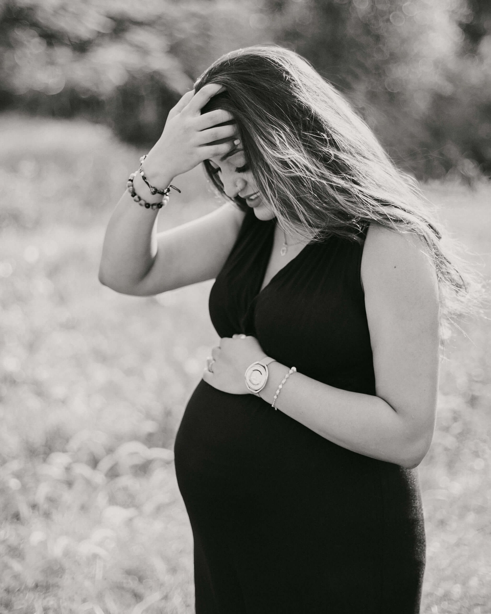 Old movie-style maternity photo, woman in elegant black gown touching her face in soft wind, Diani.