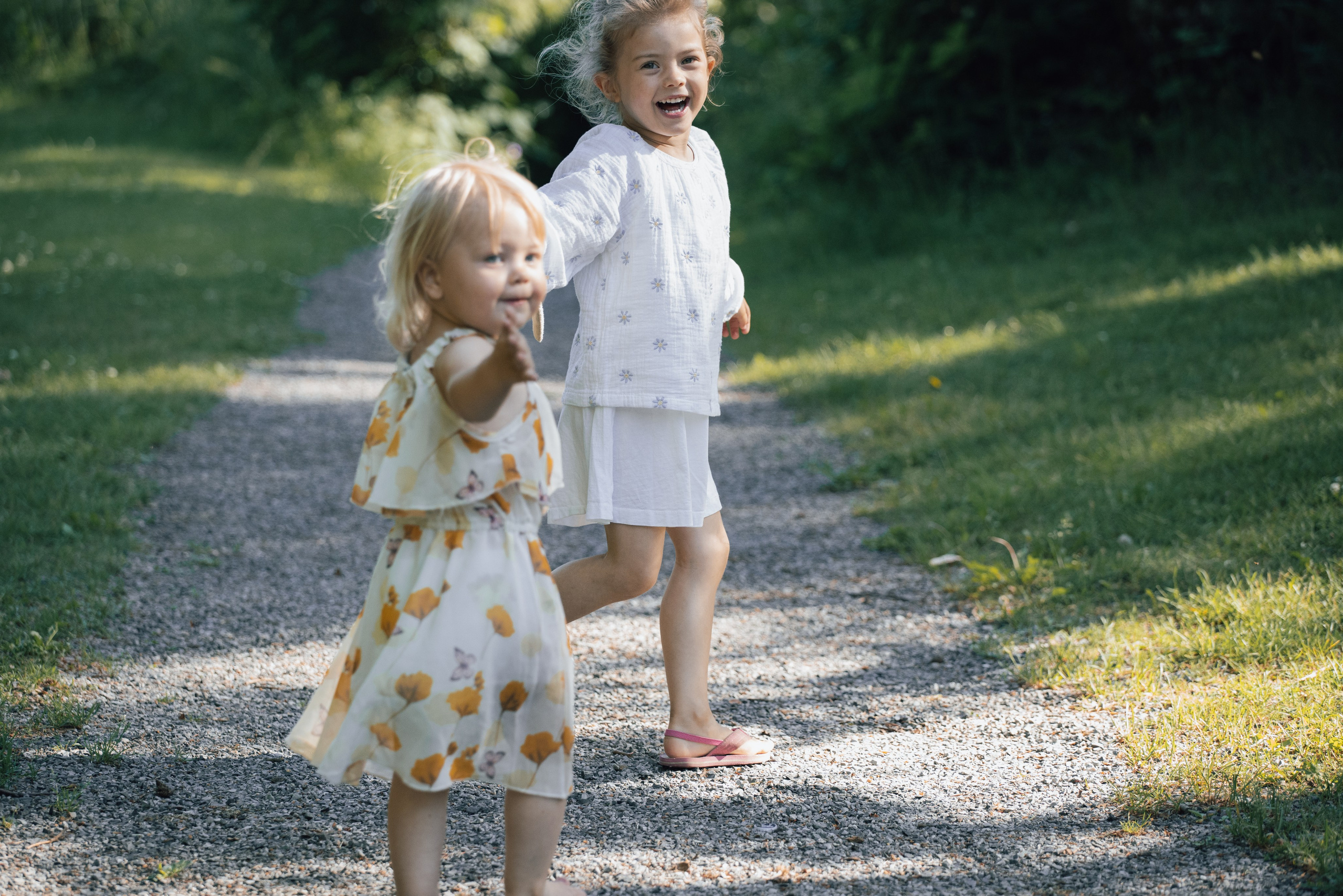 To små jenter løper i parken og ler på en sommerdag.