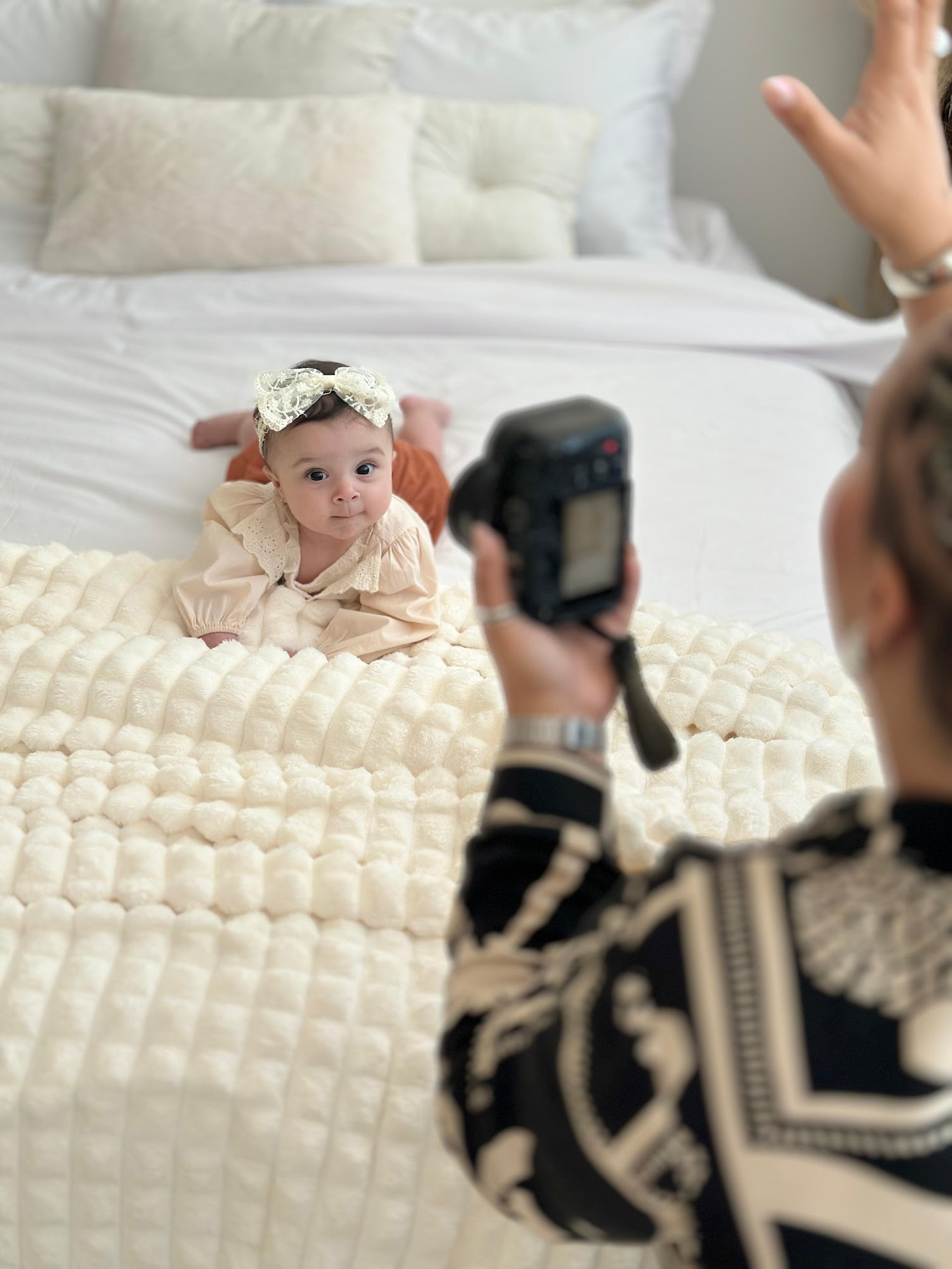 criança na cama sorrindo olhando para mãe fotografando bastidor e fotografa cortada na foto segurando a camera enquanto chama a atenção da criança