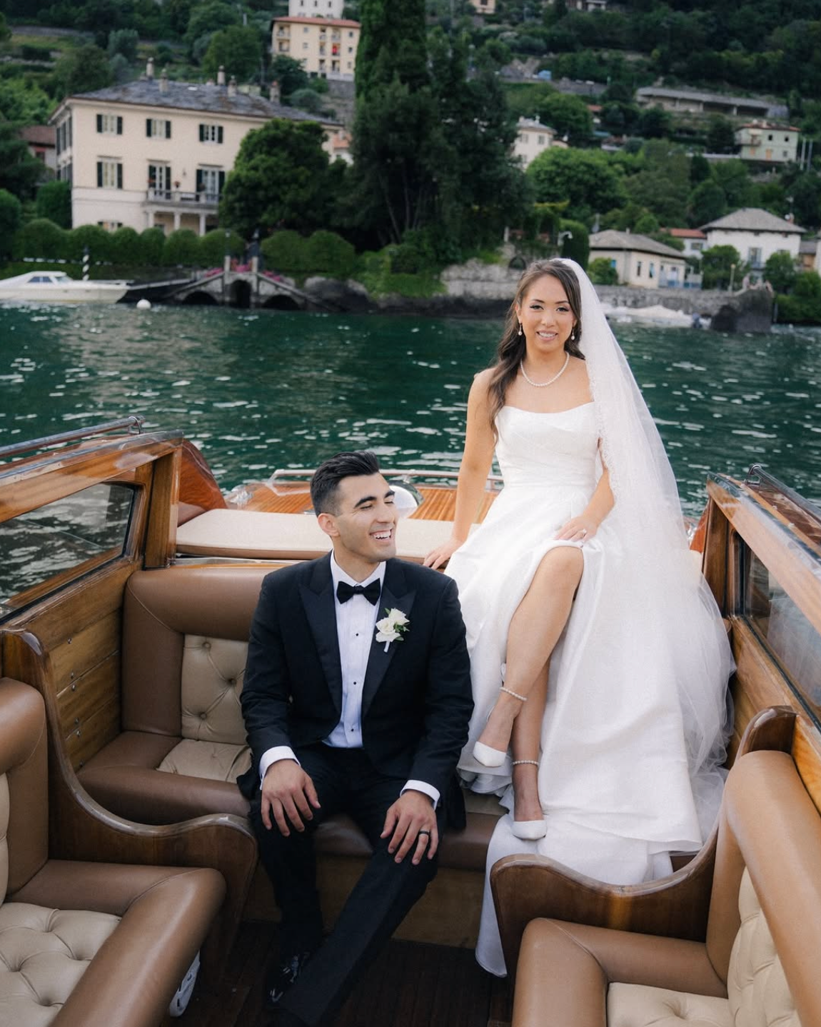 A newlywed couple walking down the aisle hand-in-hand, smiling as flower petals are thrown around them, with a floral arch and greenery in the background.