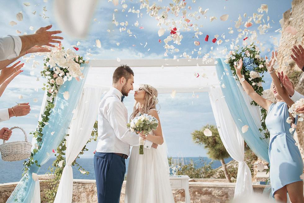 Молодоженов осыпают лепестками роз на фоне арки на Крите. Фотограф в Греции, организация свадьбы.