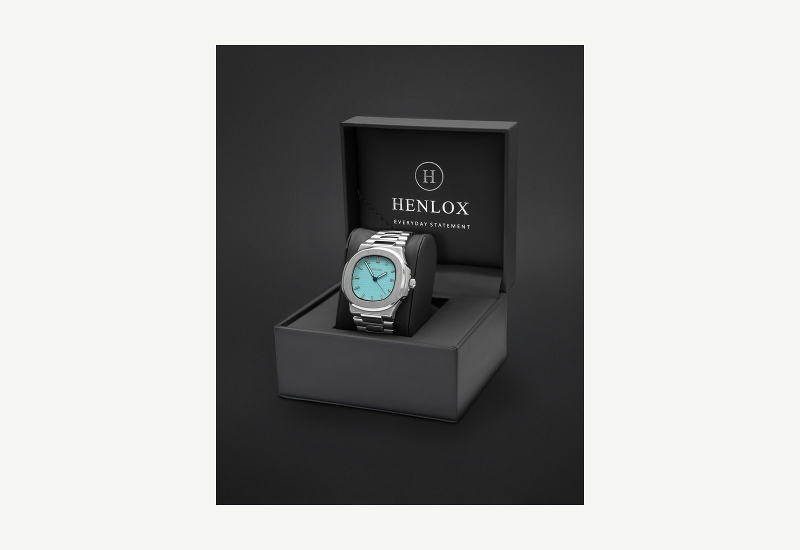 Silver-coloured wristwatch with a turquoise dial displayed in an open black presentation box