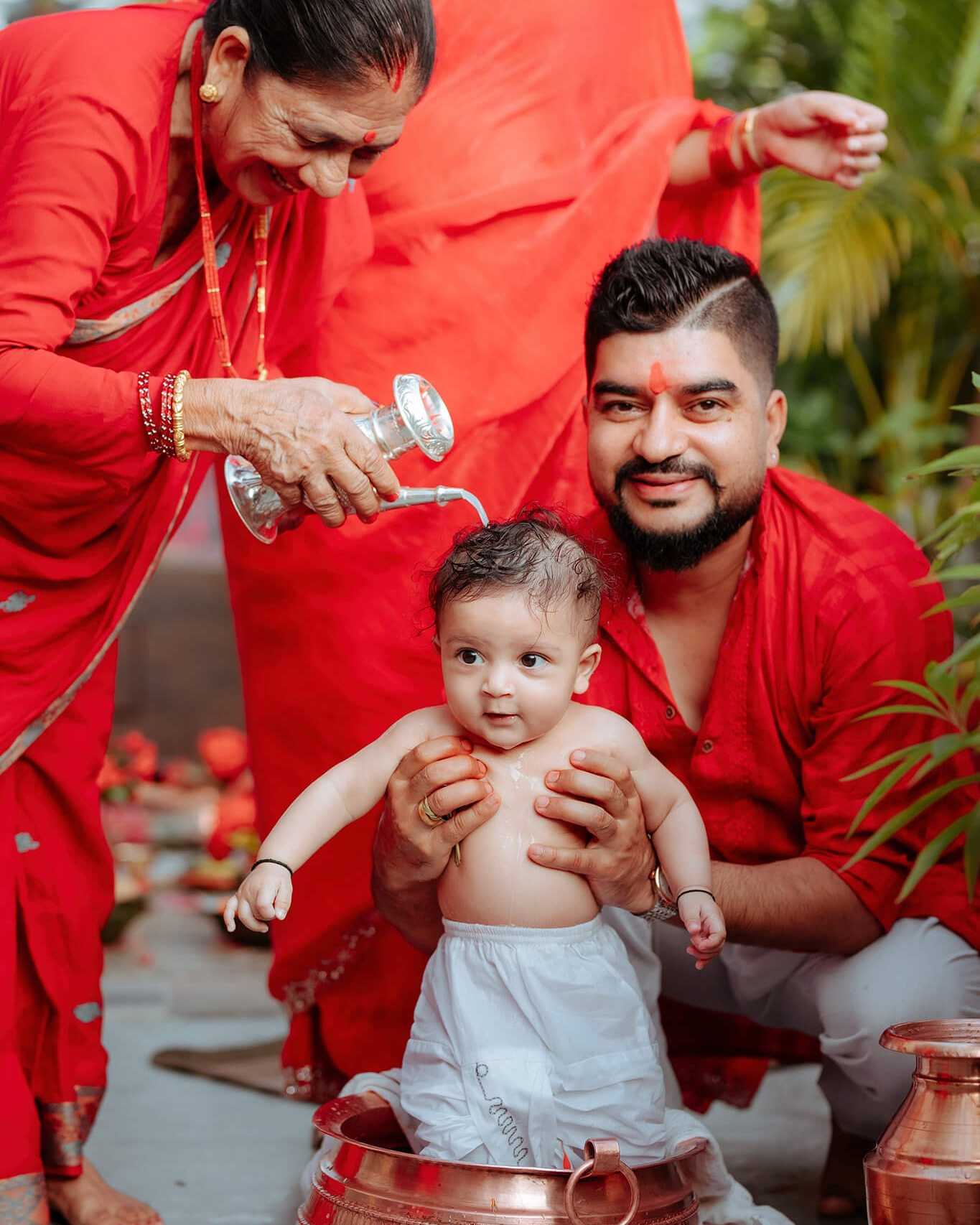 Parents in red with their baby in a copper vessel during a milk bath before the Pasni ceremony