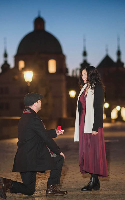 A couple dressed in vintage wedding clothes looks through the prism of a vintage camera during their Vrtba Garden pre-wedding portrait session in Prague.